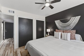 A bedroom with a bed, a ceiling fan, a wall-mounted lamp, and a decorative wall hanging. - Cozy Stylish Apt in Omaha`s Medical District! (Omaha)