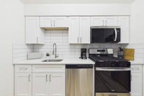 Cozinha moderna com armários brancos, micro-ondas de aço inoxidável, fogão a gás e lava-louças.
