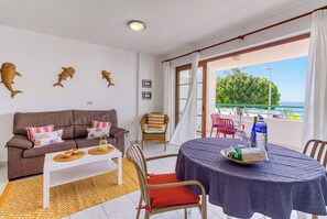 Ein Wohnbereich mit einer Couch, einem Esstisch und Stühlen, ein Balkon mit Meerblick und eine Wasserflasche auf dem Tisch.