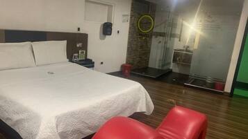 Une chambre d’hôtel avec un lit, une chaise rouge, une petite table, une table de chevet, un miroir et un espace douche.