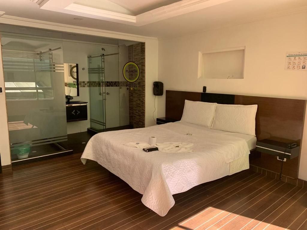 A hotel room with a bed, a nightstand, a wall-mounted phone, and a glass door leading to a shower area.
