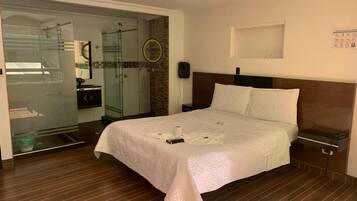 A hotel room with a bed, a nightstand, a wall-mounted phone, and a glass door leading to a shower area.