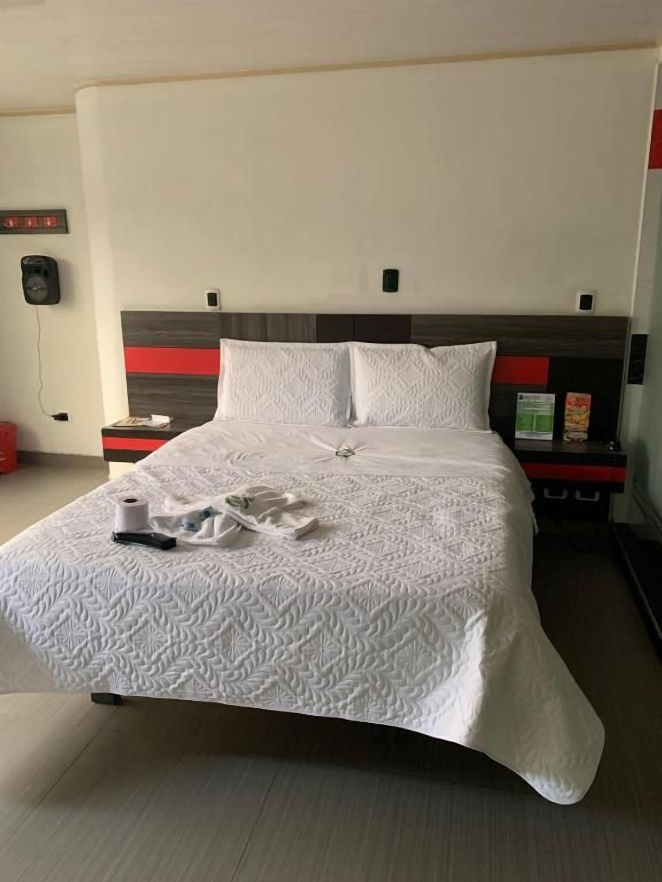 Un lit bien fait, recouvert d’une couvre-lit à motifs, une table de chevet avec une lampe et un téléphone fixé au mur.
