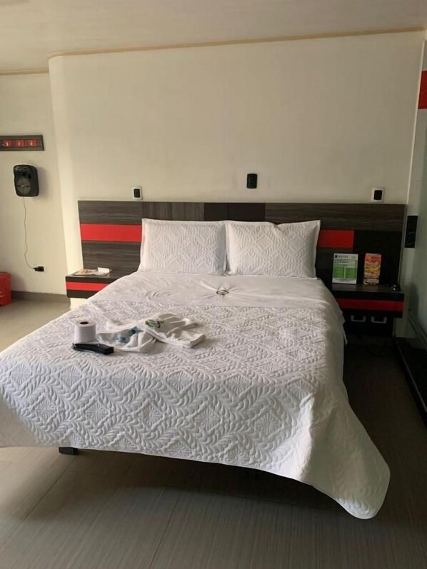 A neatly made bed with a patterned bedspread, a bedside table with a lamp, and a wall-mounted phone.
