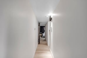 Ein schmaler Flur mit Holzboden, der zu einem Zimmer mit einem Bett und einem Nachttisch führt.