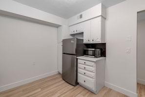 A compact kitchen with white cabinets, a stainless steel refrigerator, a microwave, and a wooden floor. - Prime Location! HGTV Design! (Omaha)