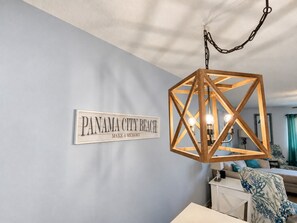 Una habitación con un cartel que dice 'PANAMA CITY BEACH MAKE A MEMORY' en la pared, una lámpara de madera con un diseño geométrico y una cama con un cojín de estampado azul y blanco.