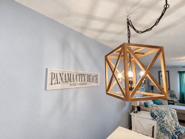 A room with a sign reading 'PANAMA CITY BEACH MAKE A MEMORY' on the wall, a wooden geometric light fixture, and a bed with a blue and white patterned pillow. - Gulf Highlands Getaway | 11 Pools + Mini Golf | Sleeps 6 (Panama City Beach)