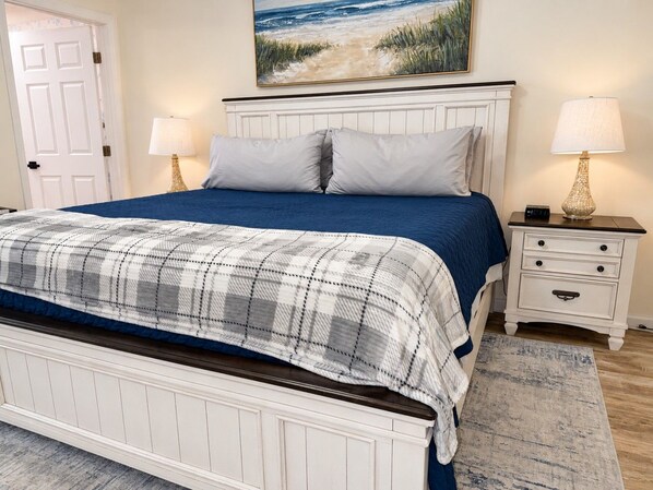 Un dormitorio con una cama, una mesita de noche, una lámpara, un cuadro y una puerta.