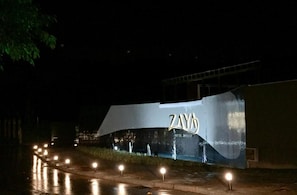 Vista nocturna de la entrada de un hotel con un gran letrero iluminado que dice 'ZAYO HOTEL PREMIUM'.