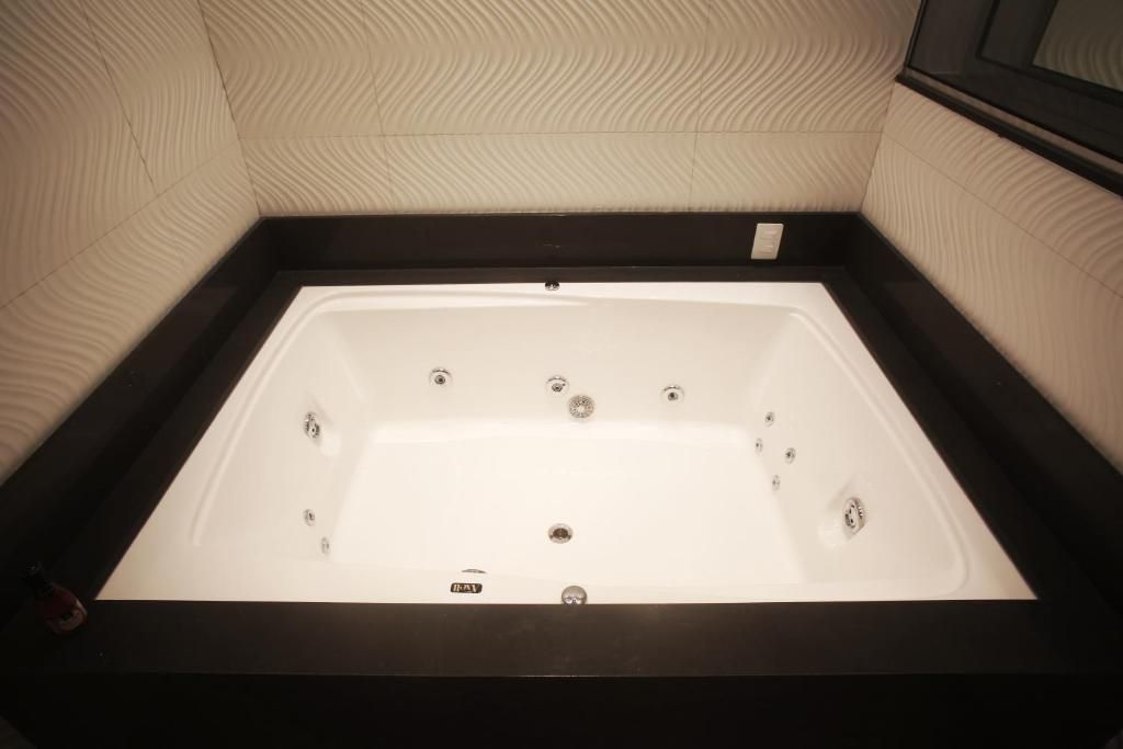 Una bañera rectangular con estructura negra, frente a una pared con textura.