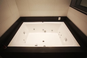 Una bañera rectangular con estructura negra, frente a una pared con textura.