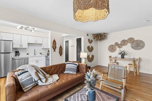 A modern living room with a brown leather sofa, a dining table with chairs, and a kitchen in the background. - Designer Mid-Term Living Near Omaha Hospitals (Omaha)