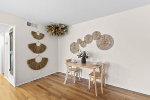 A dining area with a wooden table and chairs, a vase with flowers, and wall-mounted decorative items. - Designer Mid-Term Living Near Omaha Hospitals (Omaha)