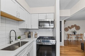 A compact kitchen with white cabinetry, a stainless steel stove, and a microwave. - Designer Mid-Term Living Near Omaha Hospitals (Omaha)