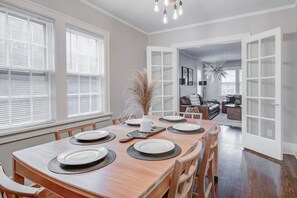 A dining area with a wooden table set for four, a vase with dried plants, and a view into a living room with a sofa and a coffee table. - Spacious Dundee Duplex | 8BR | Walk to Cafés (Omaha)
