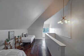 A bedroom with a sloped ceiling, a bed, a bedside table, a hanging light fixture, and a window. - Spacious Dundee Duplex | 8BR | Walk to Cafés (Omaha)
