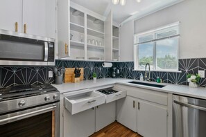 A modern kitchen with white cabinets, a stainless steel stove, and a window with blinds. - Prime Location Midtown Omaha! (Omaha)