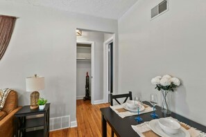 A dining area with a table set for two, a sofa, a lamp, and a vase with flowers. - Prime Location Midtown Omaha! (Omaha)