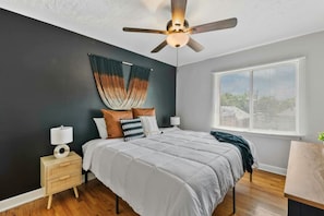 A bedroom with a bed, bedside tables, a ceiling fan, a window with blinds, and a dark wall. - Prime Location Midtown Omaha! (Omaha)