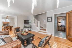 A spacious living room with a wooden floor, a black coffee table, leather sofas, and a staircase leading to another level. - Storybook Retreat | Walk to Dining & Coffee (Omaha)