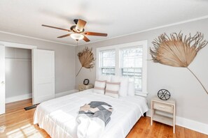 A bedroom with a bed, a ceiling fan, a nightstand, a window, and a door. - Storybook Retreat | Walk to Dining & Coffee (Omaha)