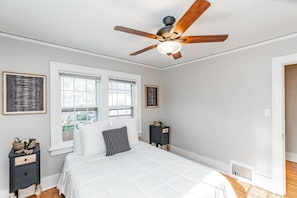 A bedroom with a bed, a ceiling fan, two windows, a nightstand, and a dresser. - Storybook Retreat | Walk to Dining & Coffee (Omaha)