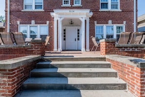 A brick building with a white entrance, numbered 5114, and a set of concrete steps leading up to it. - Storybook Retreat | Walk to Dining & Coffee (Omaha)