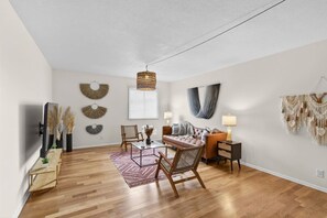 A spacious living room with a wooden floor, a brown leather sofa, a glass coffee table, and a hanging light fixture. - Designer Mid-Term Living Near Omaha Hospitals (Omaha)