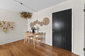 Ein Essbereich mit einem Holztisch und Stühlen, einer schwarzen Tür sowie Wanddekorationen, darunter Makramee-Wandbehänge und runde Wandbilder.