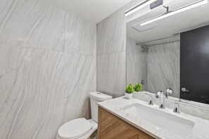 Ein modernes Badezimmer mit Marmorwänden, Toilette, Waschbecken inklusive Spiegel und Duschbereich.