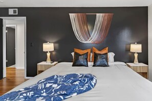 Ein modernes Schlafzimmer mit einem großen Bett, zwei Nachttischen mit Lampen, einer hängenden Textilien-Dekoration und einer Teppichdecke mit Muster.
