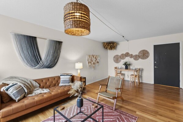 Ein Wohnzimmer mit einer Couch, einem Couchtisch, einem Sessel, einer Lampe und einem Essbereich mit Tisch und Stühlen.