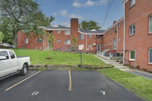A parking lot with a white pickup truck, a brick building with multiple windows and a central chimney, and a grassy area with young trees. - Prime Location Midtown Omaha (Omaha)