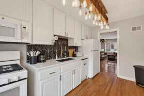 A modern kitchen with white cabinetry, a built-in microwave, a stove, and a refrigerator. There is a wooden floor and a hanging light fixture. - Prime Location Midtown Omaha (Omaha)