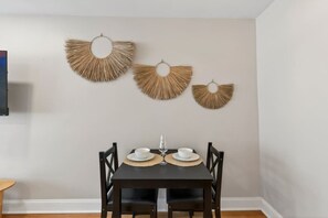 A dining area with a table set for two, featuring a dark wooden table and chairs, and a wall-mounted decorative piece above. - Prime Location Midtown Omaha (Omaha)