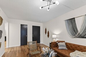 A modern living room with a brown sofa, a wooden chair, a lamp, and a ceiling light fixture. - Designer Mid-Term Living Near Omaha Hospitals (Omaha)
