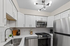 A modern kitchen with white cabinets, stainless steel appliances, a microwave, stove, oven, and a dishwasher. - Designer Mid-Term Living Near Omaha Hospitals (Omaha)