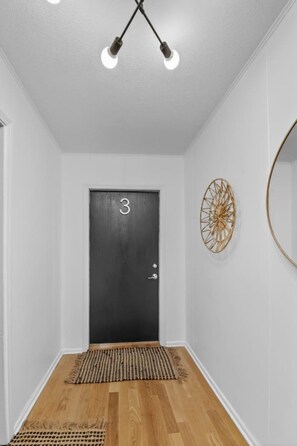 A hallway with a wooden floor, a black door with the number 3, and a wall-mounted decorative item. - Designer Mid-Term Living Near Omaha Hospitals (Omaha)