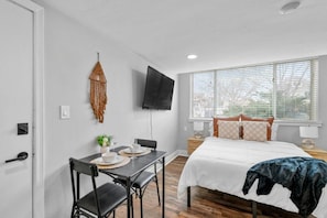 A bedroom with a bed, bedside table, TV, and a dining area with chairs and table. - Prime Location Midtown Omaha (Omaha)