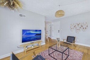 A modern living room with a flat-screen TV, wooden flooring, a patterned rug, and a woven pendant light. - Prime Location Midtown Omaha (Omaha)