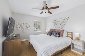 A bedroom with a bed, a ceiling fan, a TV, a bedside table, and a window. - Prime Location Midtown Omaha (Omaha)