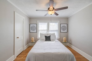 A bedroom with a bed, a ceiling fan, two windows, and framed artwork on the walls. - Storybook Retreat | Walk to Dining & Coffee (Omaha)