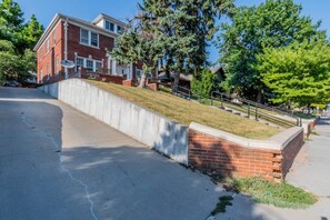 A residential area with a brick building, a concrete retaining wall, and a grassy slope. - Storybook Retreat | Walk to Dining & Coffee (Omaha)