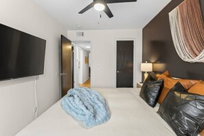 Ein Schlafzimmer mit einem Bett, einem Fernseher, einem Deckenventilator und einer Tür zu einem anderen Raum.