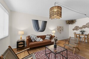 Ein modernes Wohnzimmer mit einem braunen Sofa, zwei Beistelltischen mit Lampen, einem Glastisch und einer Pendelleuchte.