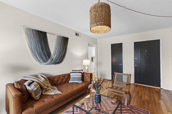 A living room with a brown leather sofa, a hanging hammock, a glass coffee table with a vase, and a wooden chair. - Designer Mid-Term Living Near Omaha Hospitals (Omaha)