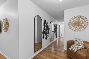 A hallway with a brown leather sofa, a patterned throw, and decorative wall art including mirrors and geometric designs. - Designer Mid-Term Living Near Omaha Hospitals (Omaha)