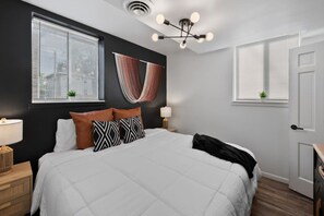 Ein Schlafzimmer mit einem großen Bett, einer Deckenleuchte, einem Fenster mit Jalousien und einer Tür.