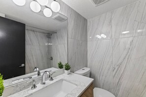 A modern bathroom with a large mirror, a sink with two faucets, a toilet, and a shower area. - Designer Mid-Term Living Near Omaha Hospitals (Omaha)
